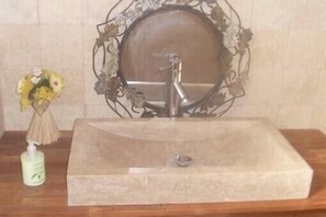 Un baño con un lavamanos rectangular, un espejo decorativo y un florero con flores.