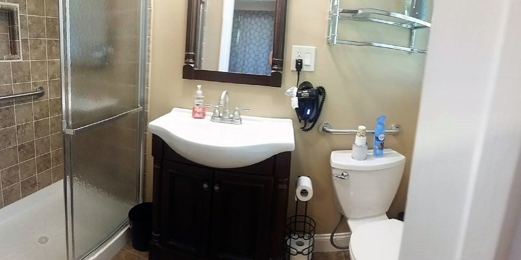 A bathroom with a white sink, dark cabinets, a mirror, a toilet, and a shower area.