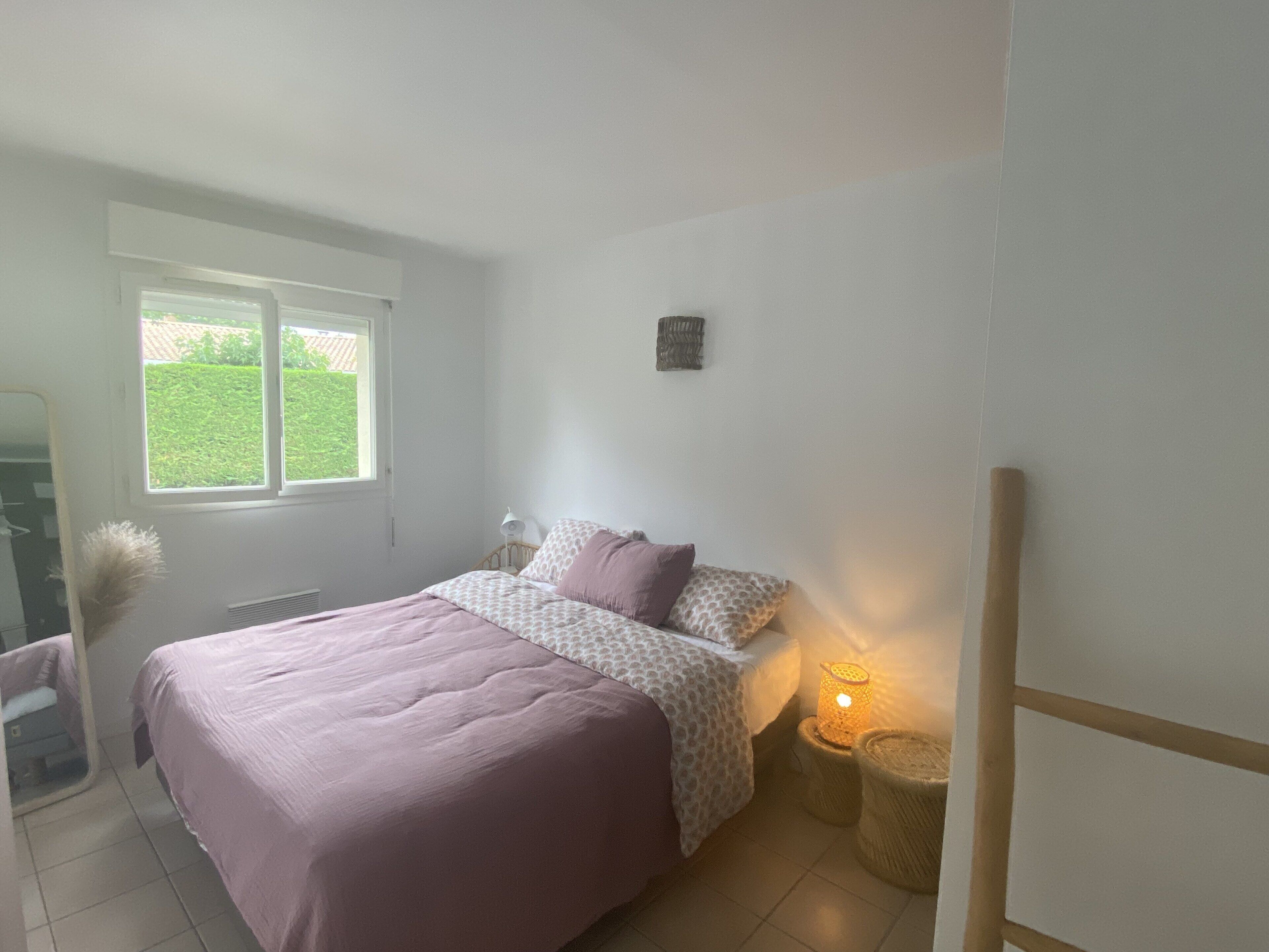 A bedroom with a bed, a window, a bedside lamp, and a small rug.