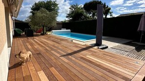 Une terrasse en bois avec une piscine, un chien et une pergola.
