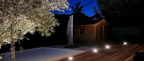 A wooden deck with a pool, a small shed, and a tree.