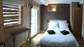 Quarto com cama, um banco, uma janela e uma porta.