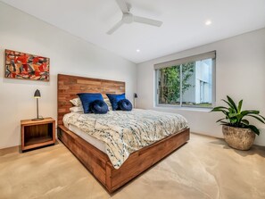 Ein modernes Schlafzimmer mit einem hölzernen Bett, einem Nachttisch, einer Stehlampe, einem Deckenventilator, einem Fenster mit Blick auf Grünflächen und einer Topfpflanze.