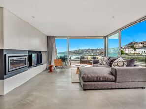 Ein modernes Wohnzimmer mit Kamin, Sofa und Blick auf eine Skyline durch große Fenster.