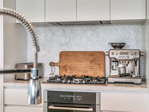 Ett kök med en Breville-espressomaskin, en skärbräda i trä, en gasspis och en Breville-diskmaskin.