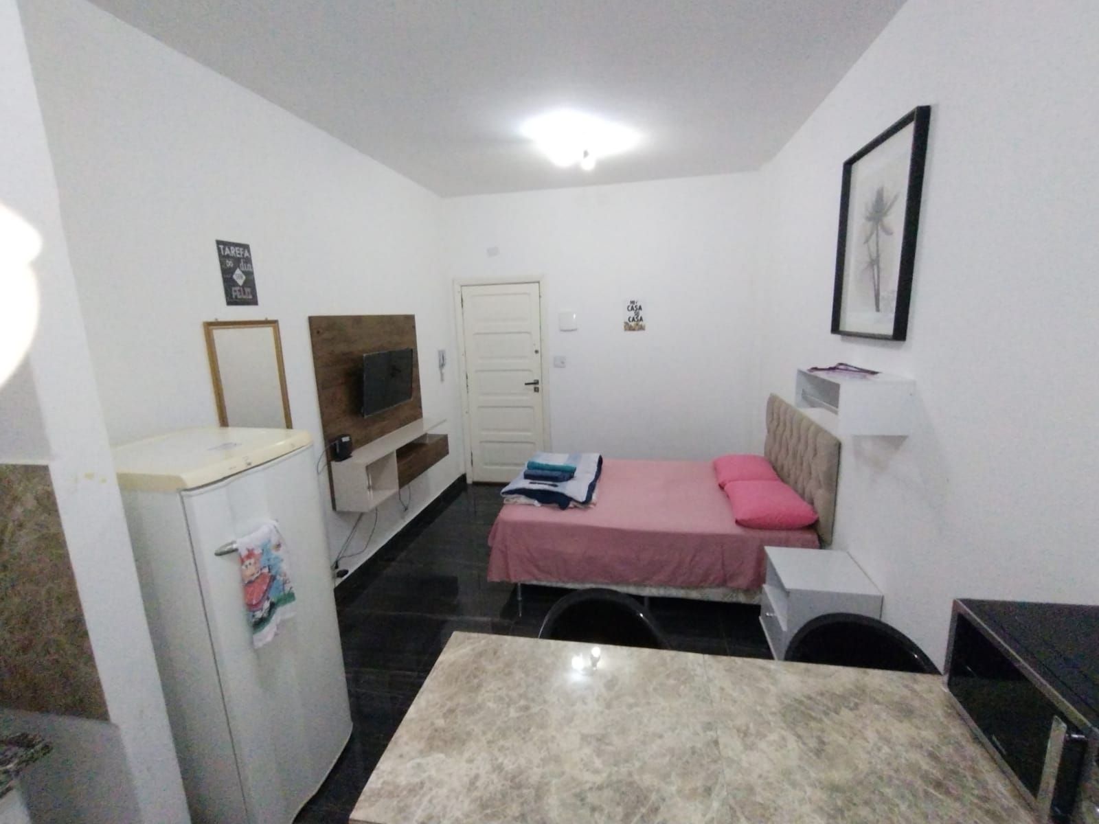 A compact room with a bed, a small desk, a television, and a refrigerator.