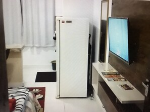 Ein Zimmer mit einem Bett, einem Fernseher, einer weißen Tür und einem kleinen Tisch mit Zeitschriften.