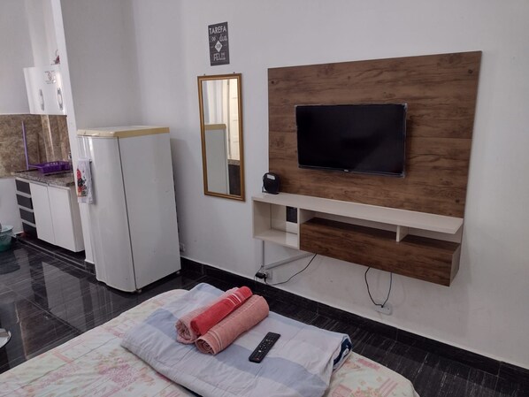 Ett hotellrum med en säng, en tv som är monterad på en träpanel, en liten hylla under tv:n och en spegel på väggen.