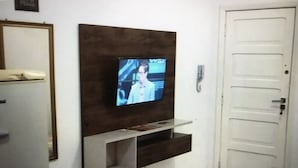 Een kamer met een aan de muur bevestigde televisie, een deur en een bed met een bedspread met een patroon.