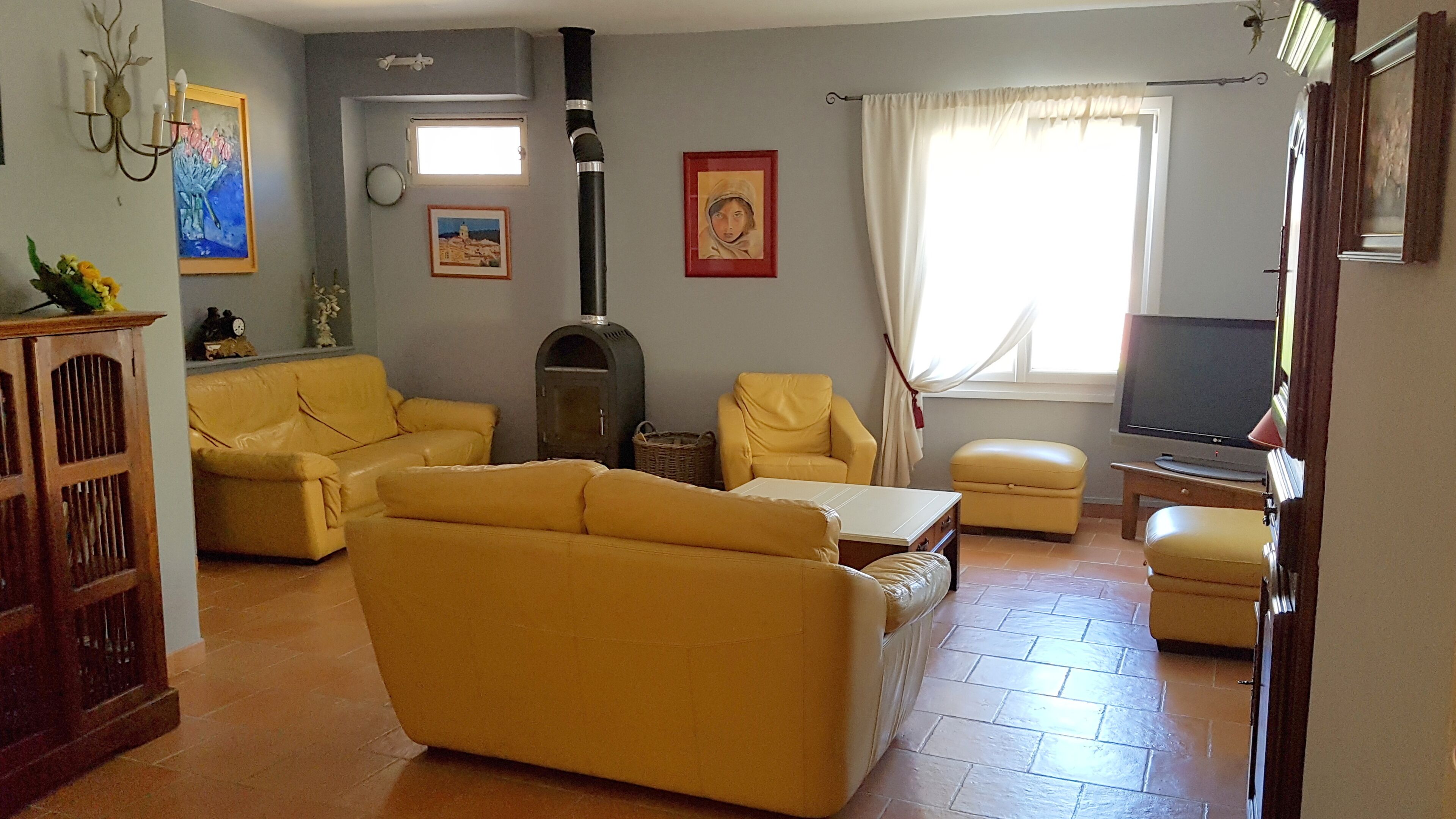 Ein Wohnzimmer mit gelben Sofas, einem Kamin, einem Fernseher und Kunstwerken an den Wänden.