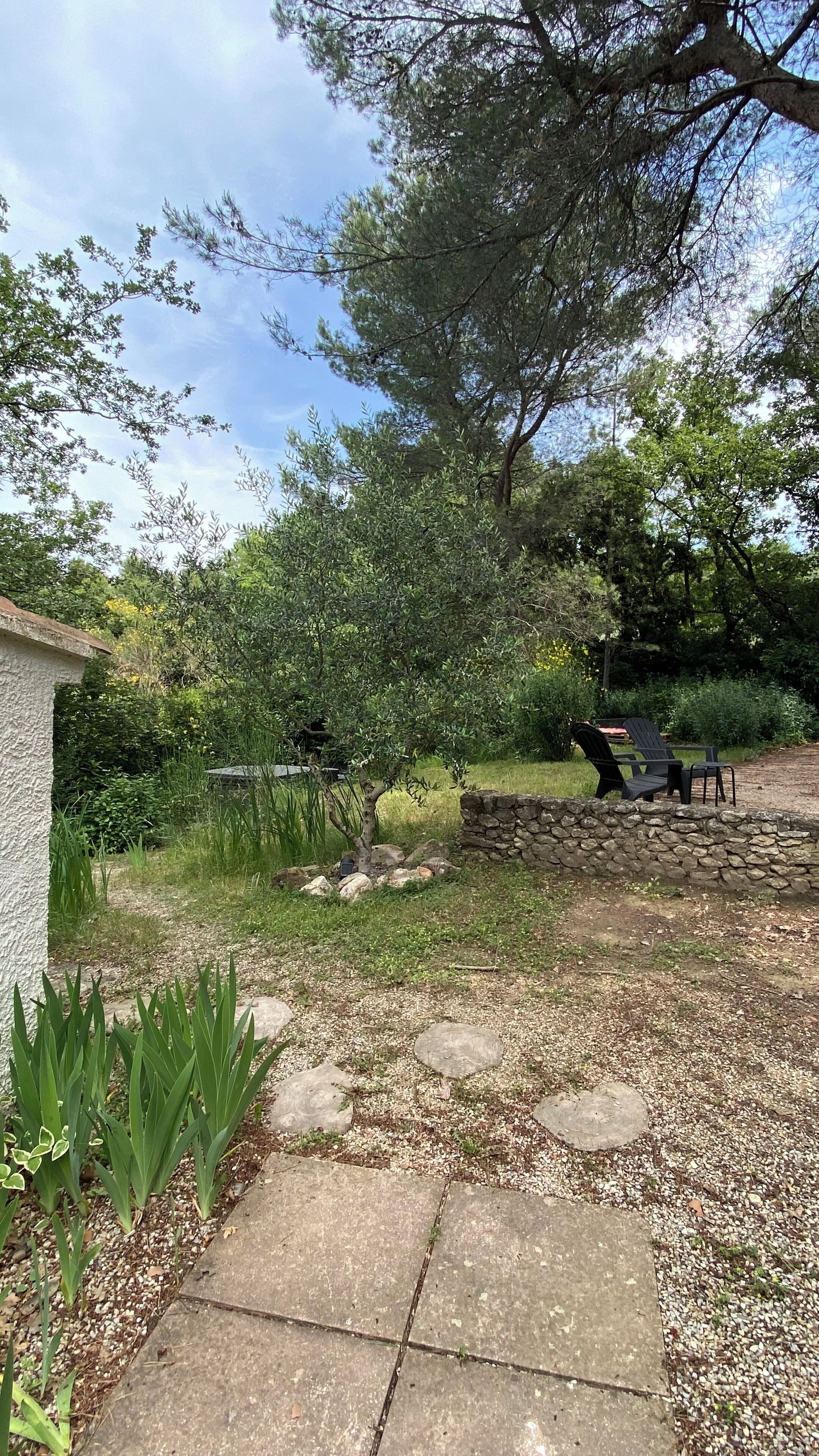 Un jardin avec un mur en pierre, un chemin dallé et un espace aménagé pour s’asseoir à l’extérieur.