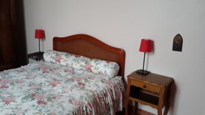 Een bed met een bloemenprint sprei, twee nachtkastjes met lampen en een decoratie aan de muur.