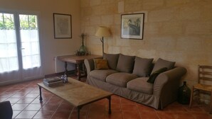 Una sala de estar con un sofá, una mesa de centro y una lámpara. Hay cuadros en la pared y una ventana con persianas.