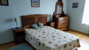 Un dormitorio con cama, cómoda, mesita de noche, lámpara y ventana.