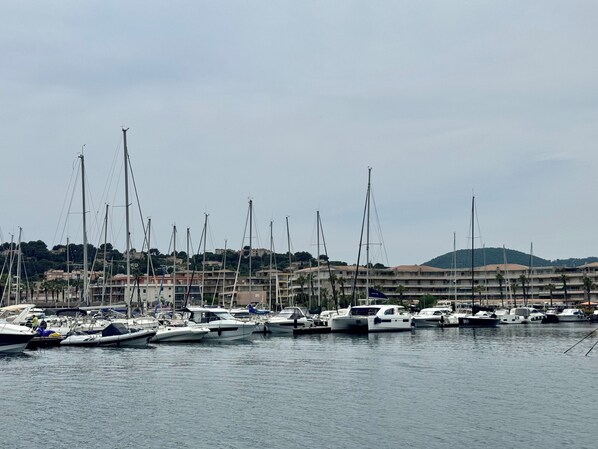 A marina with multiple boats docked, surrounded by buildings and hills in the background.