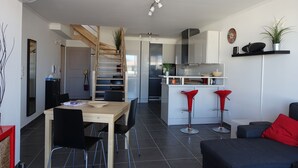 A modern kitchen with a central island, a dining area with a wooden table and chairs, and a living area with a sofa and red accents. - Rare product (T3) in the heart of Cavalaire  (Cavalaire-Sur-Mer)