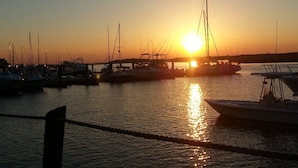 Een jachthaven in de zonsondergang, met boten afgemeerd, een heldere lucht en kalm water dat de zon weerkaatst.