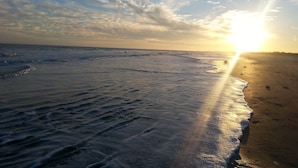 Een strand met golven en een ondergaande zon.