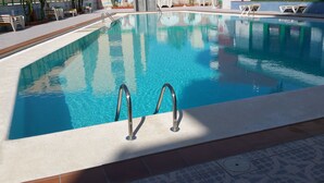 Ein Swimmingpool mit klarem, blauem Wasser, einer Fliesenveranda und Metallleiter.