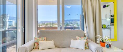 Una sala moderna con sofá, una mesita y vistas de la ciudad a través de amplias ventanas.
