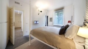 Une chambre à coucher avec un lit, une fenêtre, une lampe de chevet et une porte donnant sur une autre pièce.