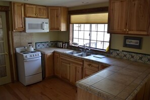 A kitchen with wooden cabinets, a white stove, a microwave, and a window with blinds. - Dragon's Lair / Garden Loft, Very Private, Cov. Gar. 1 BR. 1 BA. 1 Mi to MS. (Mt Shasta)