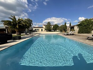 Piscina rectangular con agua azul cristalina, rodeada por una terraza de madera y sillones de descanso.