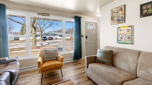 A living room with a sofa, armchair, and a view of a parking lot through large windows. - Oneida St duplex 5 min walk to Lambeau 8 beds furnished full kitchen laundry (Green Bay)