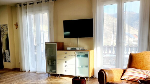 A living room with a flat-screen TV, a glass cabinet, a sofa, and a coffee table with glasses. - 68 m² *** self-contained apartment, large terrace, parking, surrounded by mountains. (Haute-Garonne)