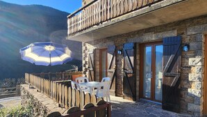 A stone building with a wooden balcony, a table with chairs, and a large umbrella. - 68 m² *** self-contained apartment, large terrace, parking, surrounded by mountains. (Haute-Garonne)