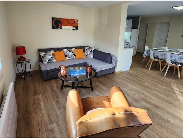 A living room with a sofa, a coffee table, and a leather armchair. There is a dining area with a table set for four.