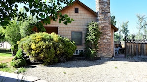 A house with a stone chimney, a wooden exterior, and a well-maintained yard with a bush and gravel path. - Cabin in Apple Orchard - Pool - Hot Tub -Farm -Breakfast -Quiet Side Zion -Bryce (Mount Carmel)