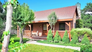 A rustic cabin with a wooden deck, surrounded by lush greenery and trees. - Cabin in Apple Orchard - Pool - Hot Tub -Farm -Breakfast -Quiet Side Zion -Bryce (Mount Carmel)