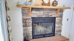 A stone fireplace with a black glass door, a wooden mantel shelf with decorative items, and a stone bench below. - Cabin in Apple Orchard - Pool - Hot Tub -Farm -Breakfast -Quiet Side Zion -Bryce (Mount Carmel)