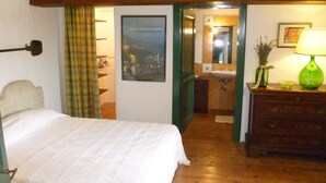 A bedroom with a bed, a green door leading to a bathroom, a wooden dresser, and a green lamp. - Cacciarella elegant and independent holiday apartment to rent  2+2 pax (Arezzola)