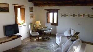 A cozy living room with a flat-screen TV, a dining table with chairs, a sofa, and a large window with wooden shutters. - Cacciarella elegant and independent holiday apartment to rent  2+2 pax (Arezzola)