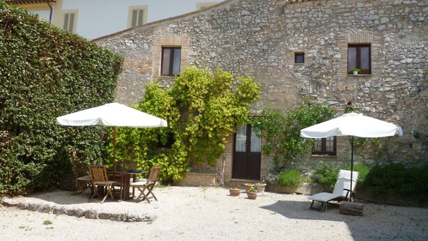 A courtyard with stone walls, outdoor seating, and umbrellas. - Cacciarella elegant and independent holiday apartment to rent  2+2 pax (Arezzola)