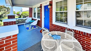 A covered porch with a blue door, white outdoor furniture, and a patterned rug.