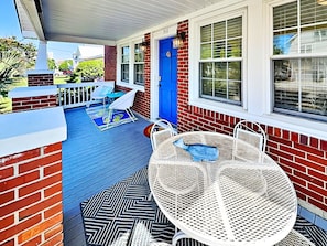A covered porch with a blue door, white outdoor furniture, and a patterned rug.