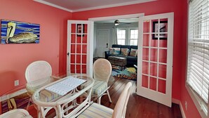 A room with a dining table, chairs, a painting, a sofa, and a window with blinds.