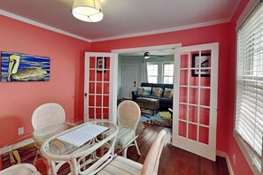 Une pièce comprenant une table à manger, des chaises, un tableau, un canapé et une fenêtre avec des stores.