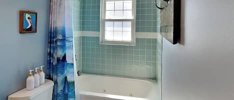 A bathroom with a bathtub, toilet, and a window.