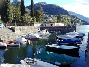 A marina with several boats docked, a stone wall, and a building with arched windows in the background. - Charming romantic apartment in an ancient villa in Bellagio, close to lakeshore (Bellagio)