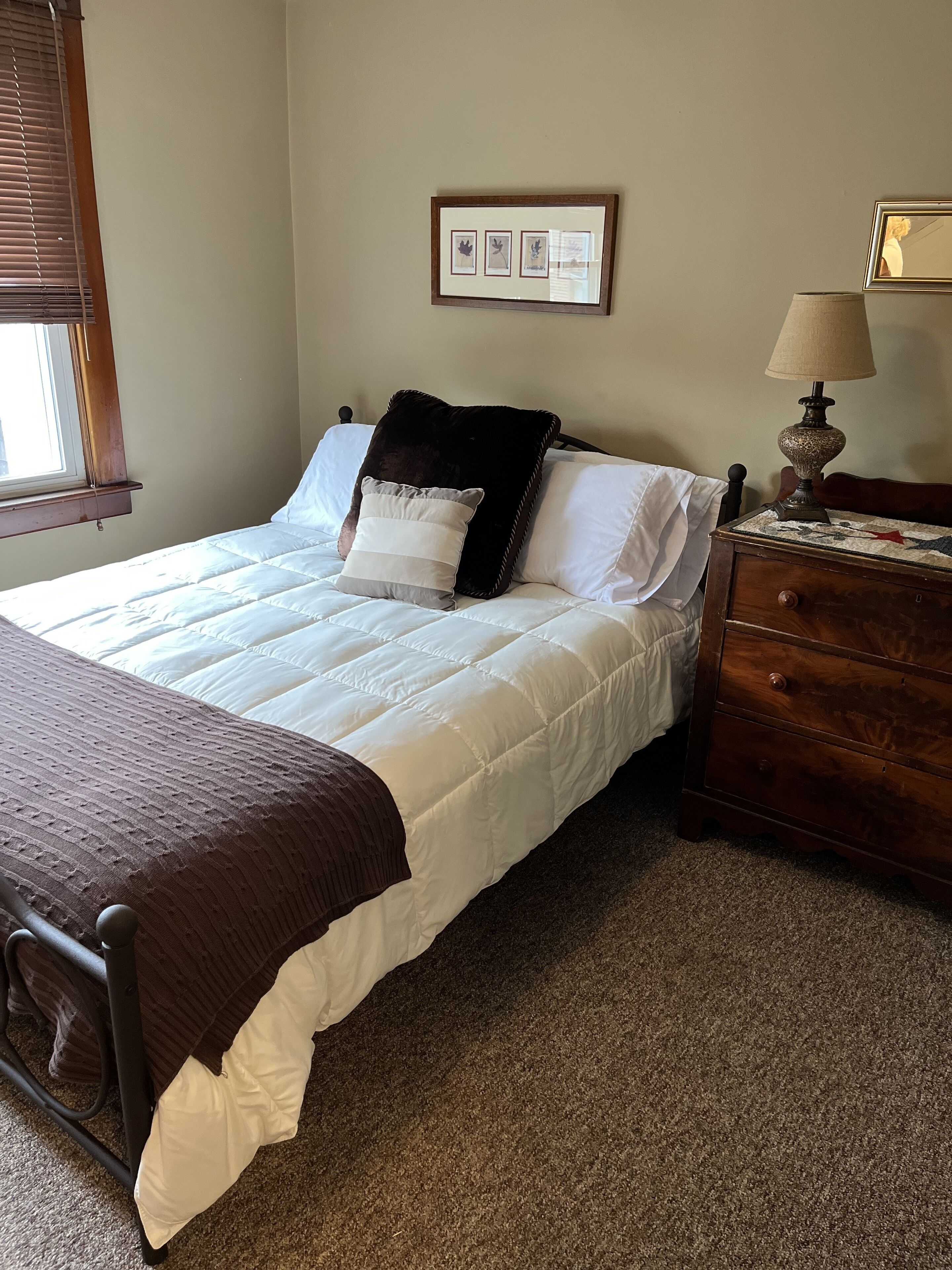 A neatly made bed with white and brown bedding, a wooden nightstand with a lamp, and a framed picture on the wall.