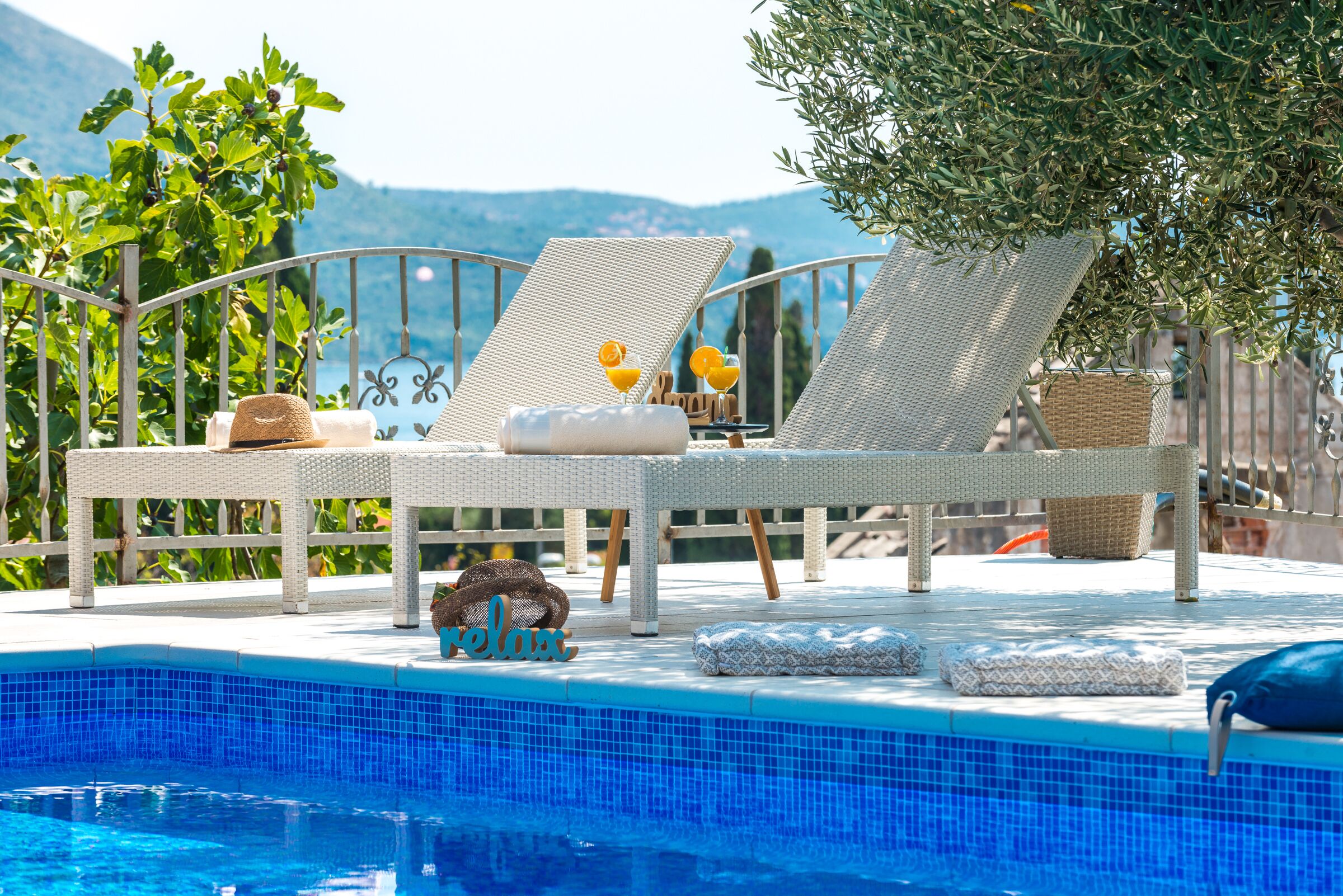 Un espace aménagé au bord de la piscine, avec des chaises longues, un chapeau, un panier et un coussin orné du mot «détente».