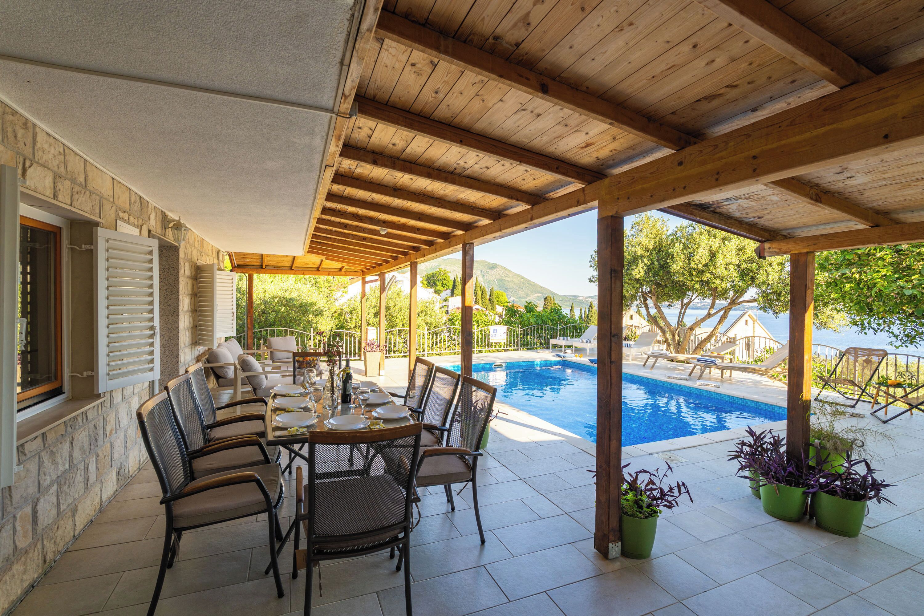 An outdoor patio with a pool, wooden pergola, and seating area.