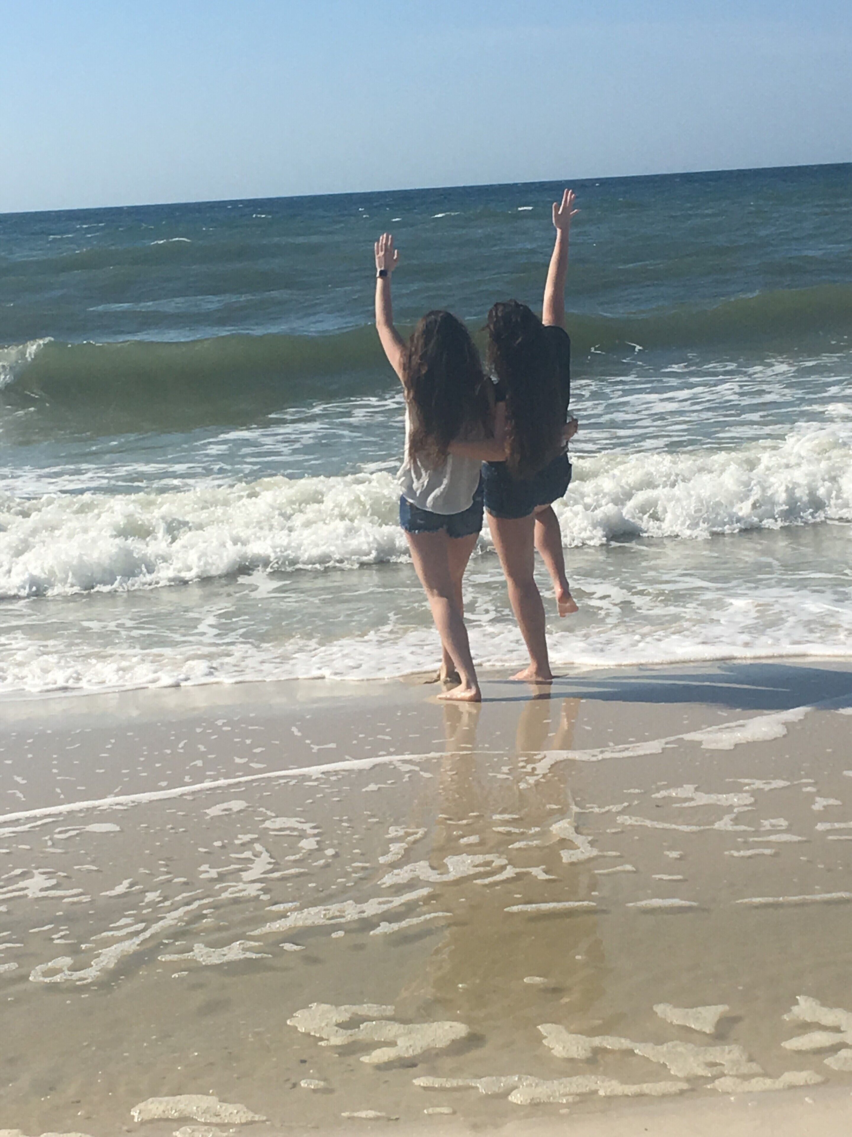 Two people standing on a beach with their arms raised, facing the ocean.