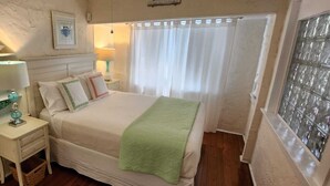 Une chambre à coucher comprenant un lit, des tables de chevet, une étagère avec des objets décoratifs, une fenêtre avec des rideaux et un luminaire fixé au mur.