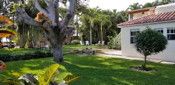 A well-maintained garden with a patio area, a small tree, and a white building with a red-tiled roof.
