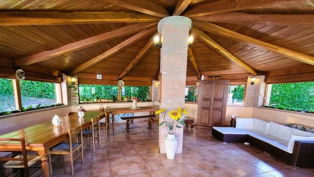 An indoor patio with a wooden ceiling, a long dining table, a sofa, and a potted plant. - Private pool, WIFI, walking distance facilities. Electric car charging point (Castiglione di Garfagnana)